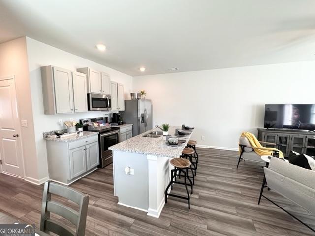 kitchen featuring a kitchen bar, light stone counters, appliances with stainless steel finishes, gray cabinets, and an island with sink