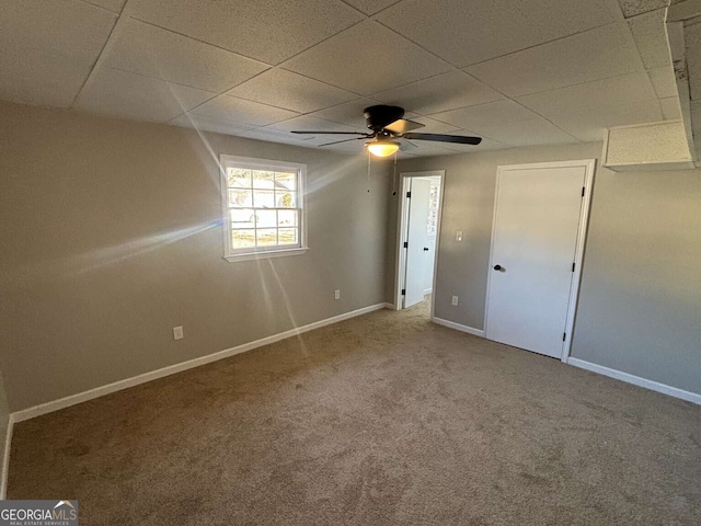 unfurnished bedroom featuring a ceiling fan, a paneled ceiling, baseboards, and carpet