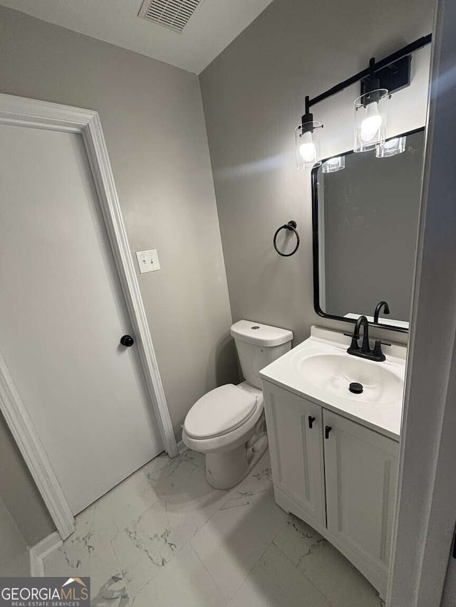 half bathroom featuring toilet, marble finish floor, vanity, and visible vents