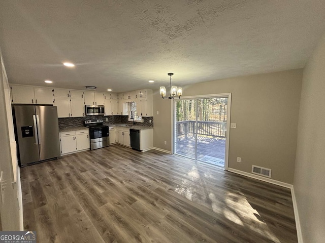 kitchen with stainless steel appliances, visible vents, white cabinets, decorative backsplash, and decorative light fixtures