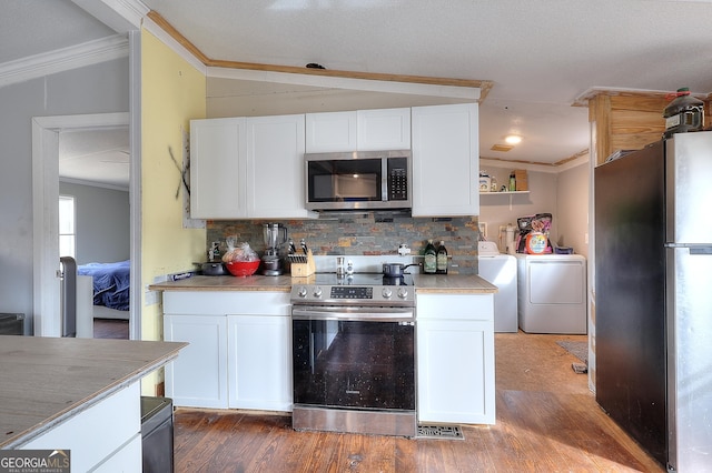 kitchen with stainless steel appliances, washing machine and dryer, ornamental molding, and white cabinets