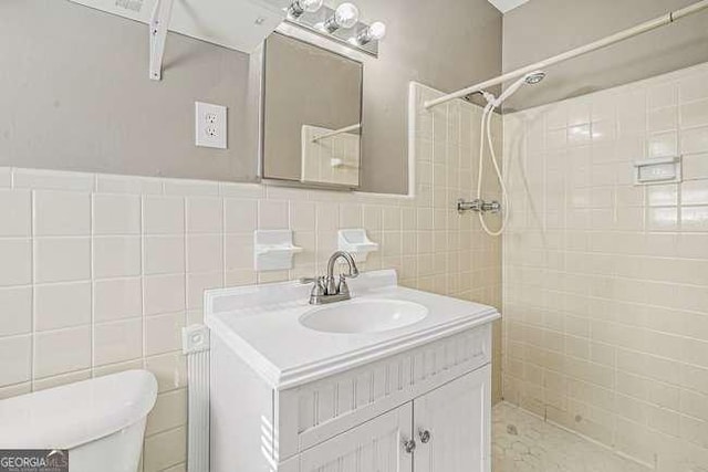 bathroom with tile walls, vanity, toilet, and a tile shower