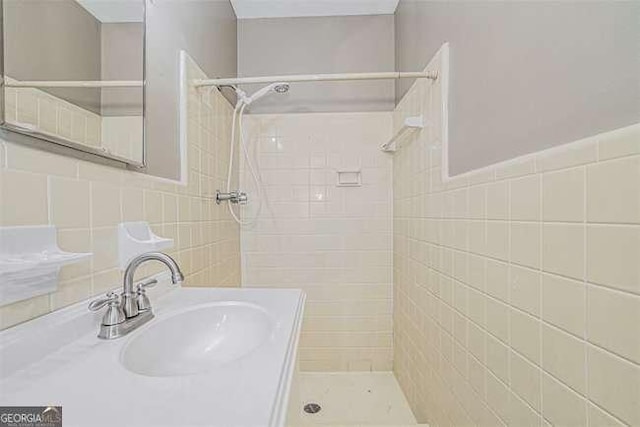 bathroom featuring a tile shower, sink, and tile walls