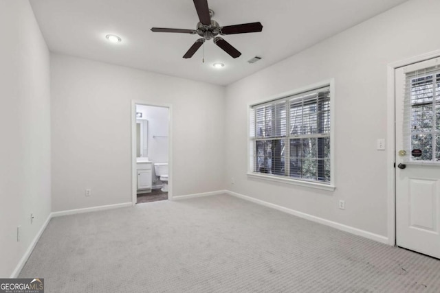 unfurnished bedroom with ceiling fan, multiple windows, ensuite bath, and light carpet