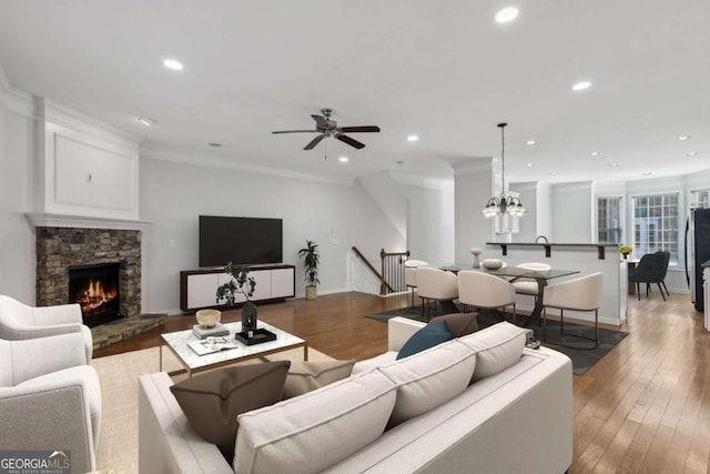 living room featuring crown molding, wood-type flooring, a stone fireplace, and ceiling fan