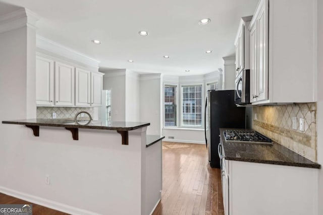 kitchen with a breakfast bar area, white cabinetry, appliances with stainless steel finishes, dark hardwood / wood-style floors, and dark stone counters