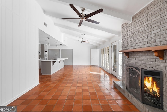 unfurnished living room with lofted ceiling with beams, sink, ceiling fan, a brick fireplace, and tile patterned floors