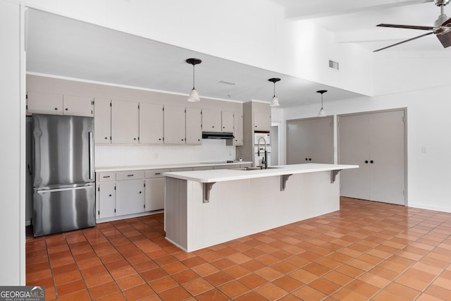 kitchen with lofted ceiling with beams, hanging light fixtures, stainless steel fridge, an island with sink, and ceiling fan