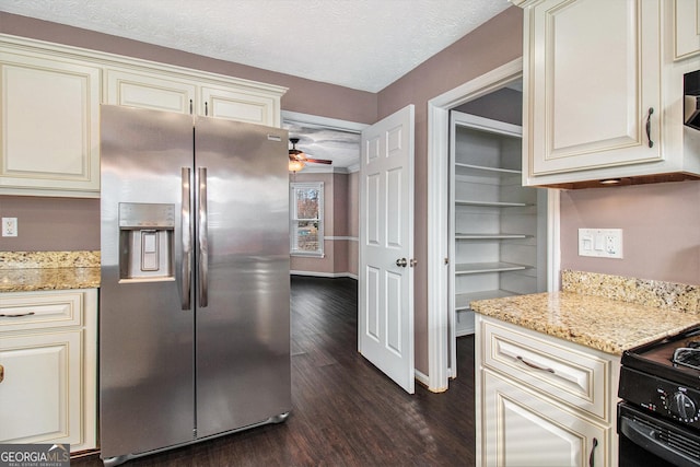 kitchen with light stone counters, cream cabinets, stainless steel fridge, and a textured ceiling