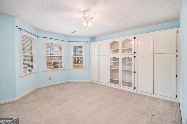 unfurnished bedroom with ceiling fan, light carpet, and a textured ceiling