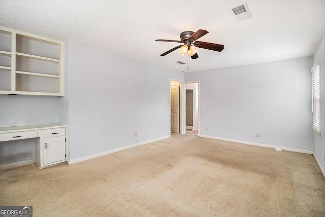 empty room with light carpet, a textured ceiling, built in desk, and ceiling fan