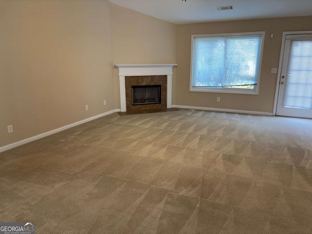 unfurnished living room with light colored carpet, a high end fireplace, and vaulted ceiling