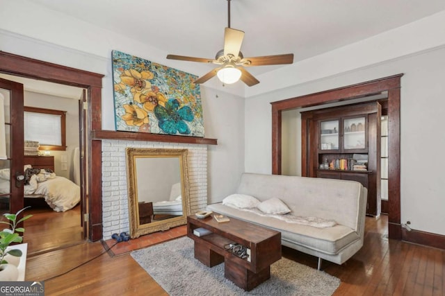 living room with a brick fireplace, dark wood-type flooring, and ceiling fan