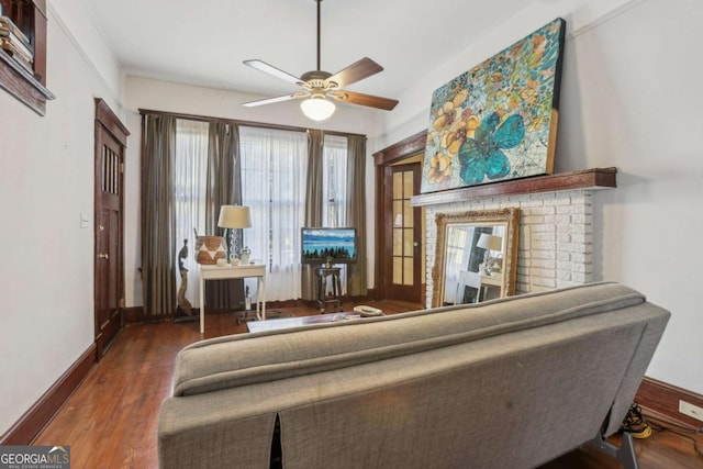 living area featuring a brick fireplace, dark hardwood / wood-style floors, and ceiling fan