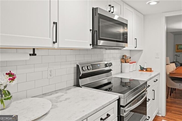 kitchen with light stone counters, appliances with stainless steel finishes, light hardwood / wood-style floors, and white cabinets