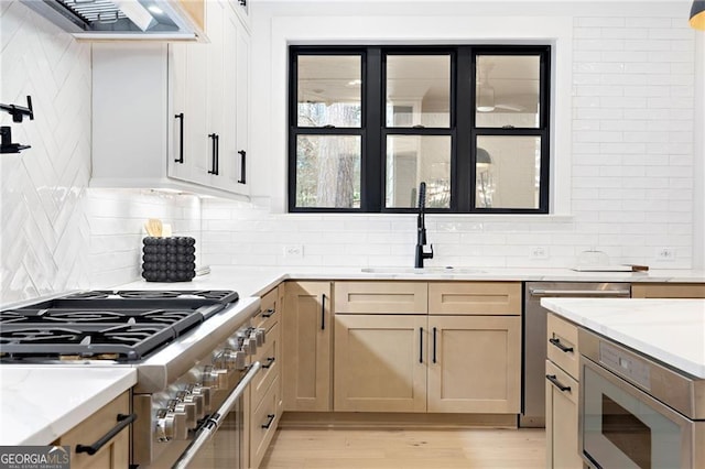 kitchen with extractor fan, sink, backsplash, light stone counters, and light wood-type flooring