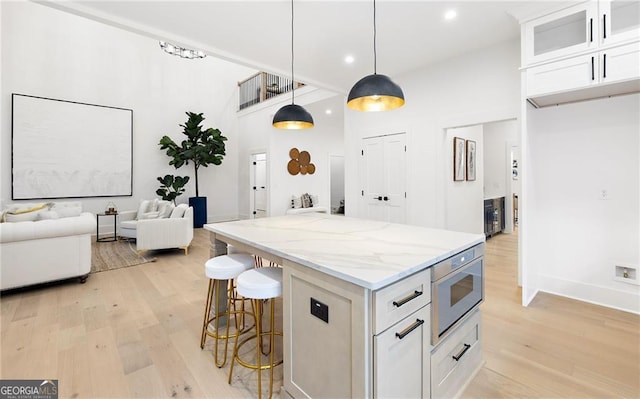 kitchen with white cabinetry, light stone counters, stainless steel microwave, a kitchen island, and decorative light fixtures