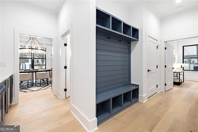 mudroom with an inviting chandelier, crown molding, and light hardwood / wood-style flooring