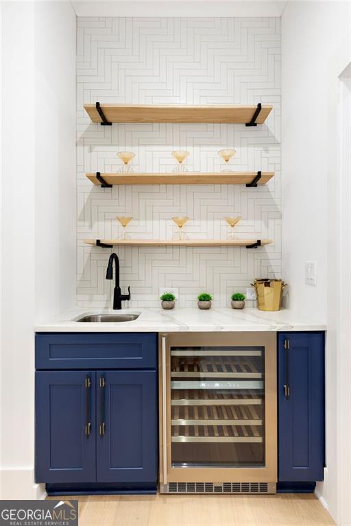 bar featuring sink, backsplash, light stone counters, blue cabinets, and beverage cooler