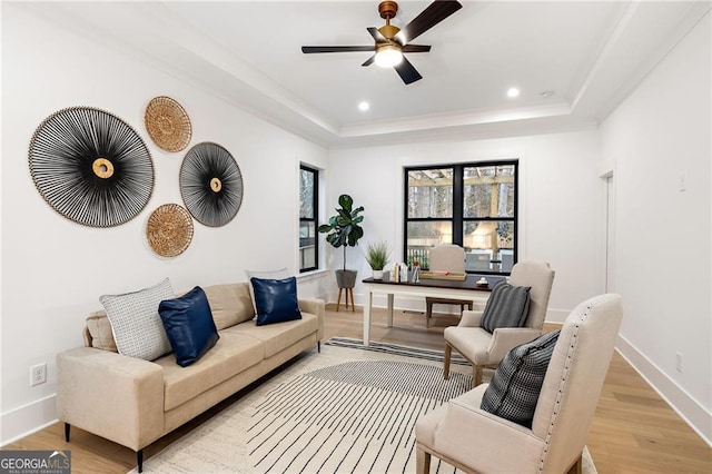 living room featuring ceiling fan, a tray ceiling, and light hardwood / wood-style flooring