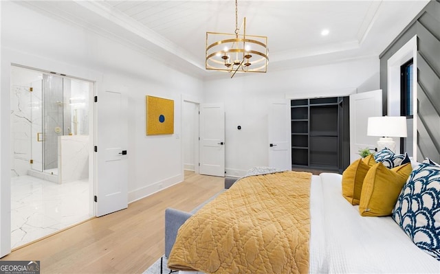 bedroom featuring crown molding, ensuite bath, a chandelier, light wood-type flooring, and a tray ceiling