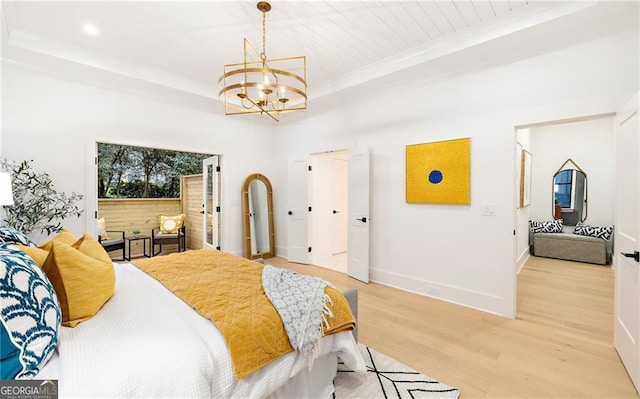 bedroom with an inviting chandelier, light wood-type flooring, and a tray ceiling