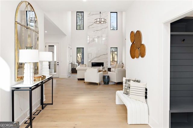 living room with a notable chandelier, a premium fireplace, light hardwood / wood-style floors, and a high ceiling