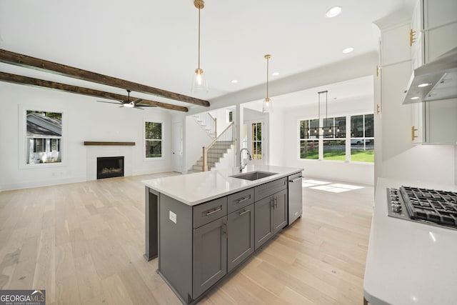 kitchen with gray cabinets, sink, hanging light fixtures, stainless steel dishwasher, and a center island with sink