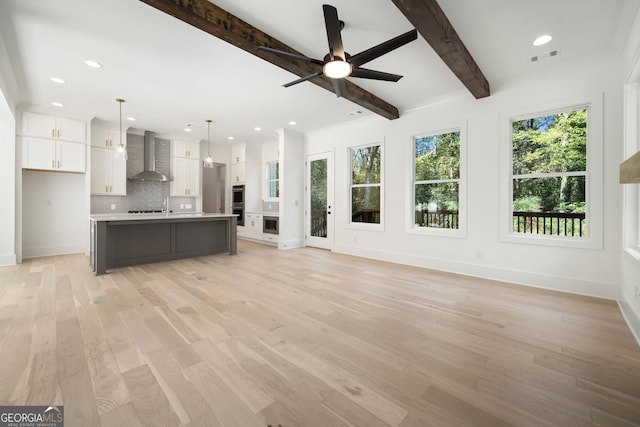 unfurnished living room featuring beam ceiling, light hardwood / wood-style flooring, and ceiling fan