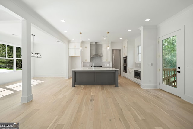 kitchen featuring wall chimney range hood, a kitchen island with sink, hanging light fixtures, tasteful backsplash, and white cabinets