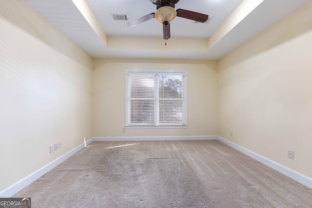 unfurnished room featuring ceiling fan, light colored carpet, and a tray ceiling