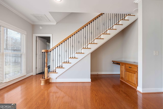 stairway with ornamental molding and hardwood / wood-style floors