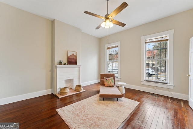 sitting room featuring dark hardwood / wood-style flooring, a brick fireplace, and ceiling fan