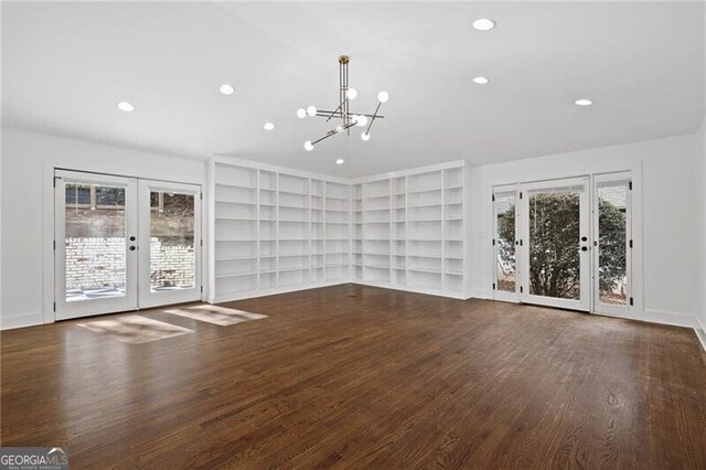 unfurnished living room with french doors, plenty of natural light, dark hardwood / wood-style floors, and an inviting chandelier