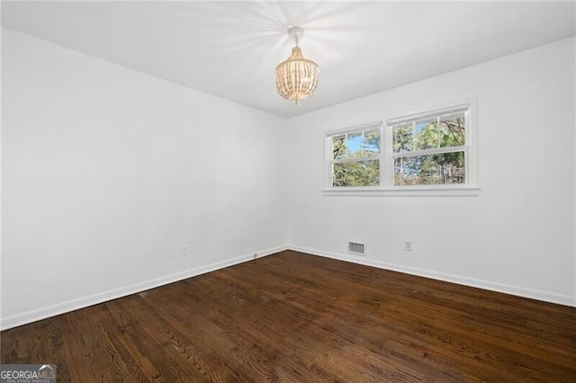 spare room with hardwood / wood-style floors and an inviting chandelier