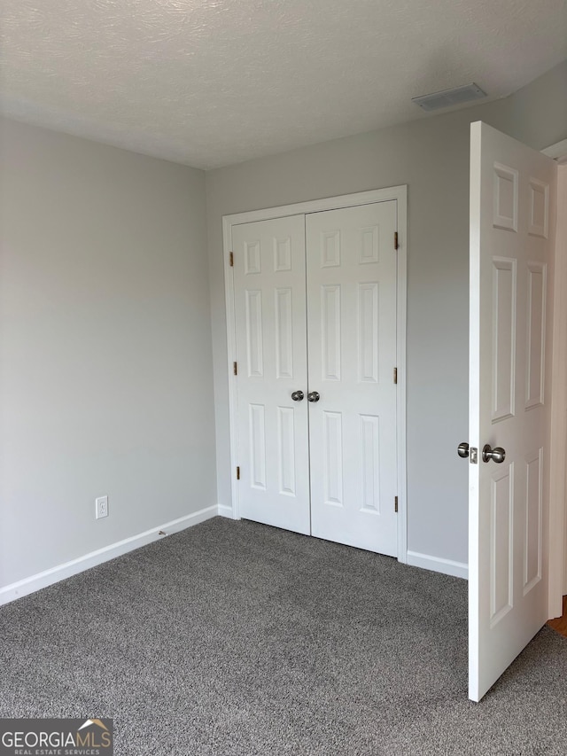 unfurnished bedroom featuring dark carpet, a closet, and a textured ceiling