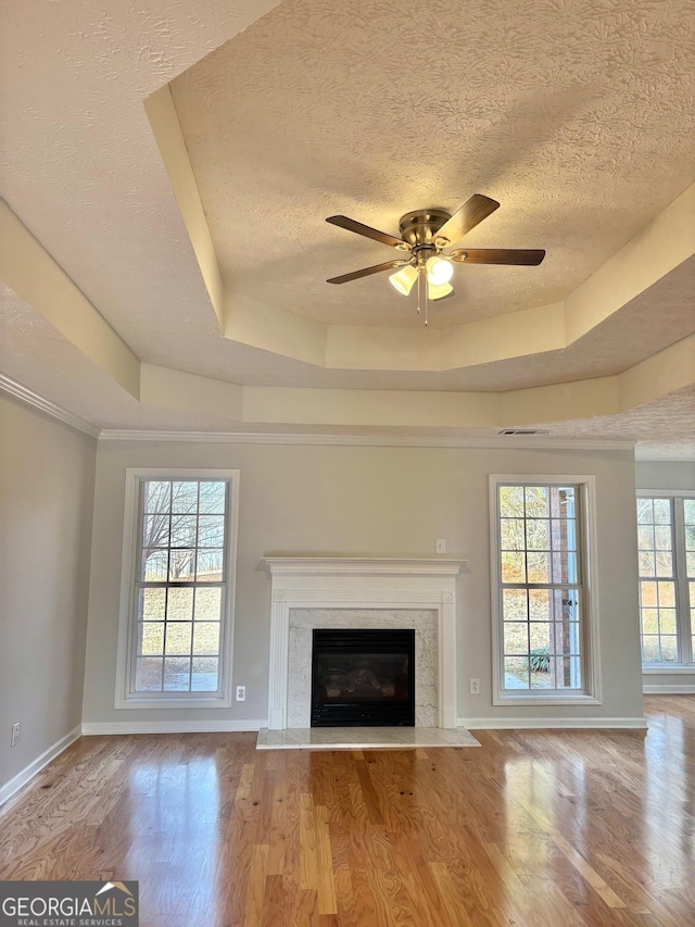 unfurnished living room with light hardwood / wood-style flooring, a textured ceiling, a fireplace, and a tray ceiling