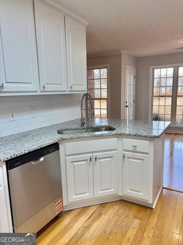 kitchen with sink, dishwasher, white cabinetry, light stone counters, and light wood-type flooring