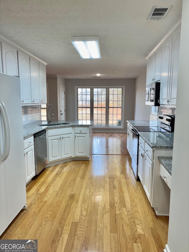 kitchen featuring sink, light wood-type flooring, kitchen peninsula, stainless steel appliances, and white cabinets