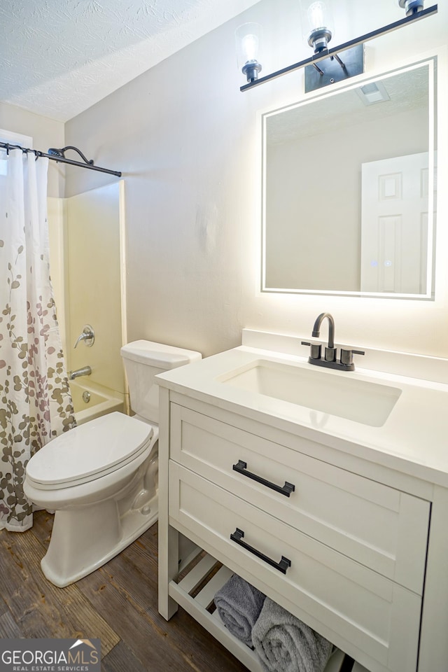 full bathroom with hardwood / wood-style floors, vanity, toilet, shower / bath combo, and a textured ceiling