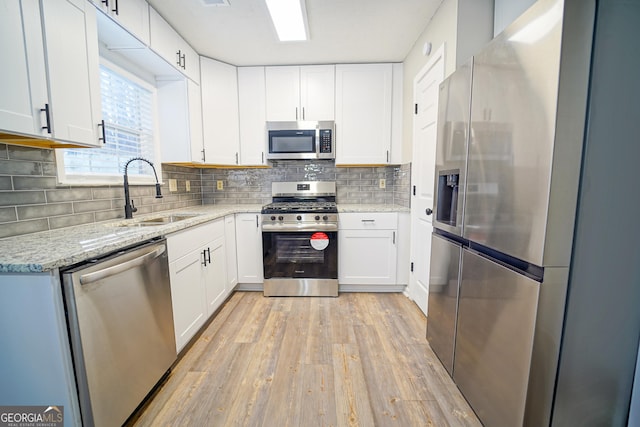 kitchen featuring appliances with stainless steel finishes, sink, white cabinets, light stone counters, and light hardwood / wood-style floors