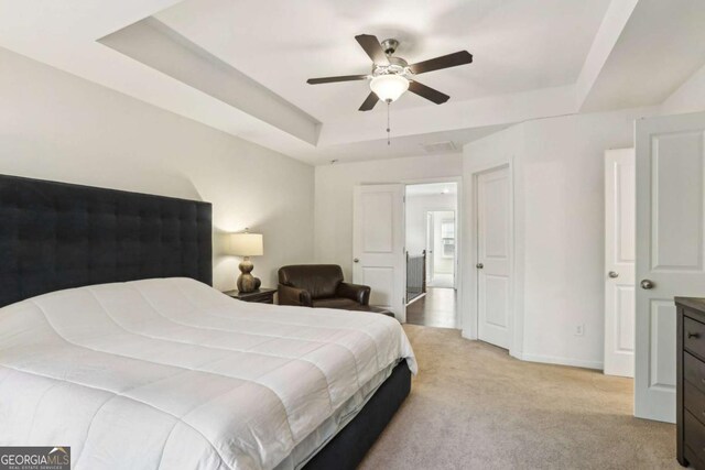 carpeted bedroom with ceiling fan and a tray ceiling