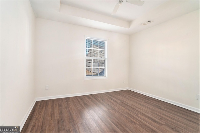 spare room with dark hardwood / wood-style flooring, a raised ceiling, and ceiling fan