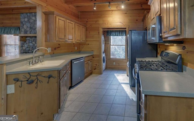 kitchen featuring sink, light tile patterned floors, wooden walls, and stainless steel appliances