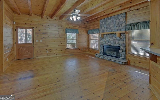 unfurnished living room with beamed ceiling, a stone fireplace, light hardwood / wood-style floors, and wood walls