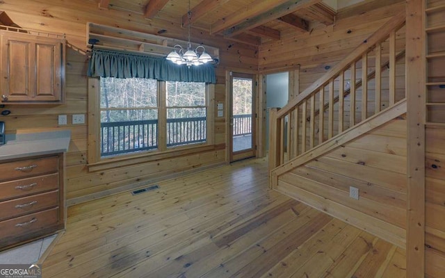 unfurnished dining area featuring wood ceiling, light hardwood / wood-style flooring, wooden walls, a notable chandelier, and beamed ceiling