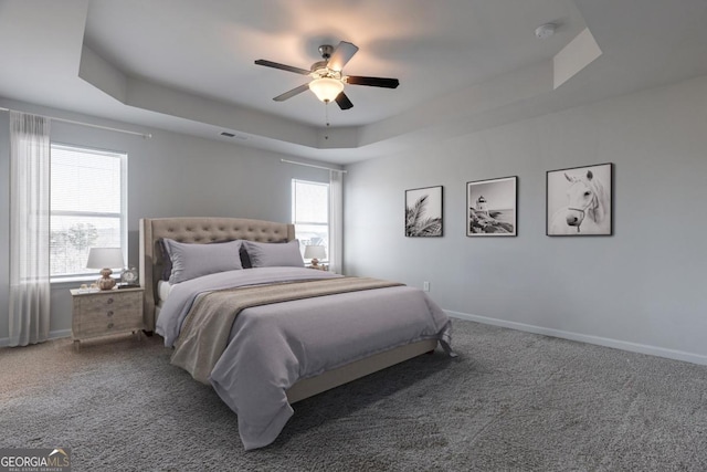 carpeted bedroom with ceiling fan and a tray ceiling