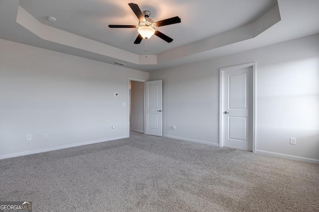 carpeted empty room with a raised ceiling and ceiling fan