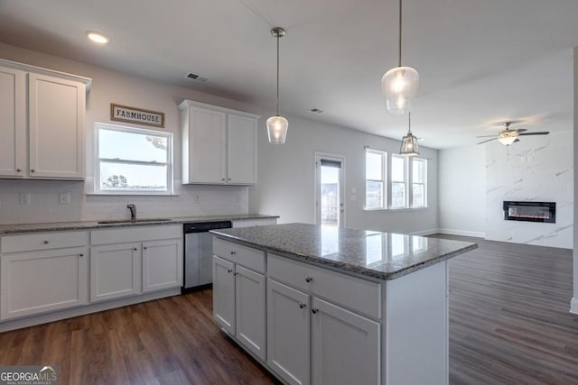 kitchen with sink, white cabinetry, hanging light fixtures, stainless steel dishwasher, and light stone countertops