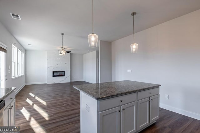 kitchen featuring dark stone countertops, a center island, pendant lighting, and a fireplace